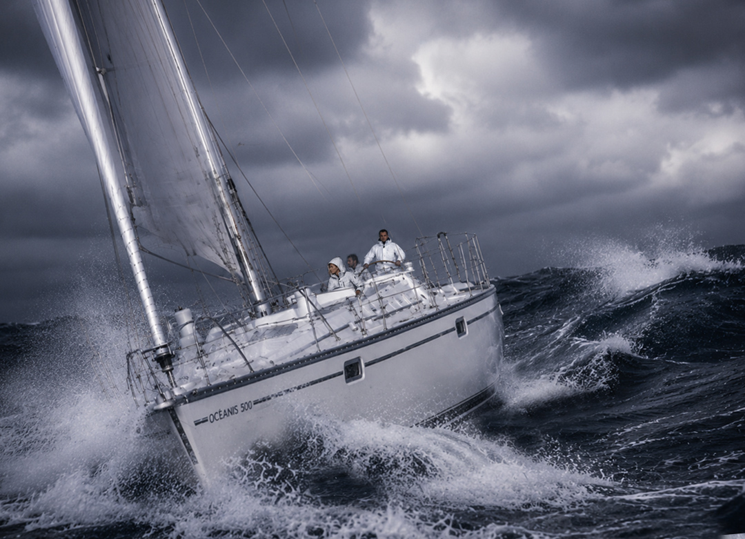 Océanis 500 naviguant dans une mer formée en Atlantique, avec un équipage en ciré blanc affrontant les vagues et les embruns.