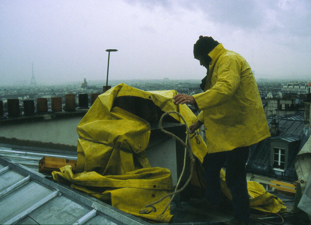 Un couvreur sur les toits de Paris met une bache sur son chantier pour protéger de la pluie